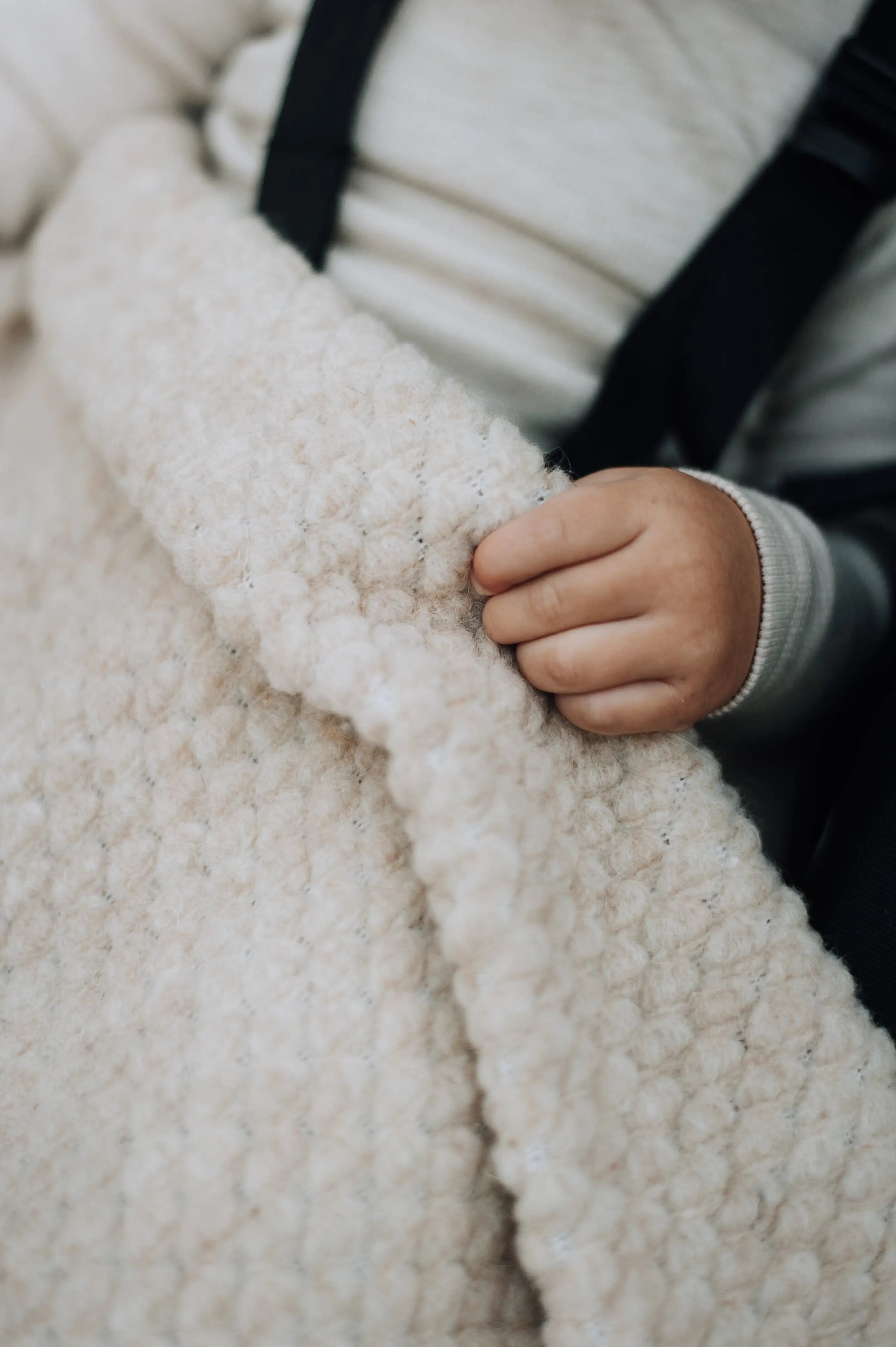 ingezoomde foto van baby hand die rand van wollen boucle deken vasthoudt
