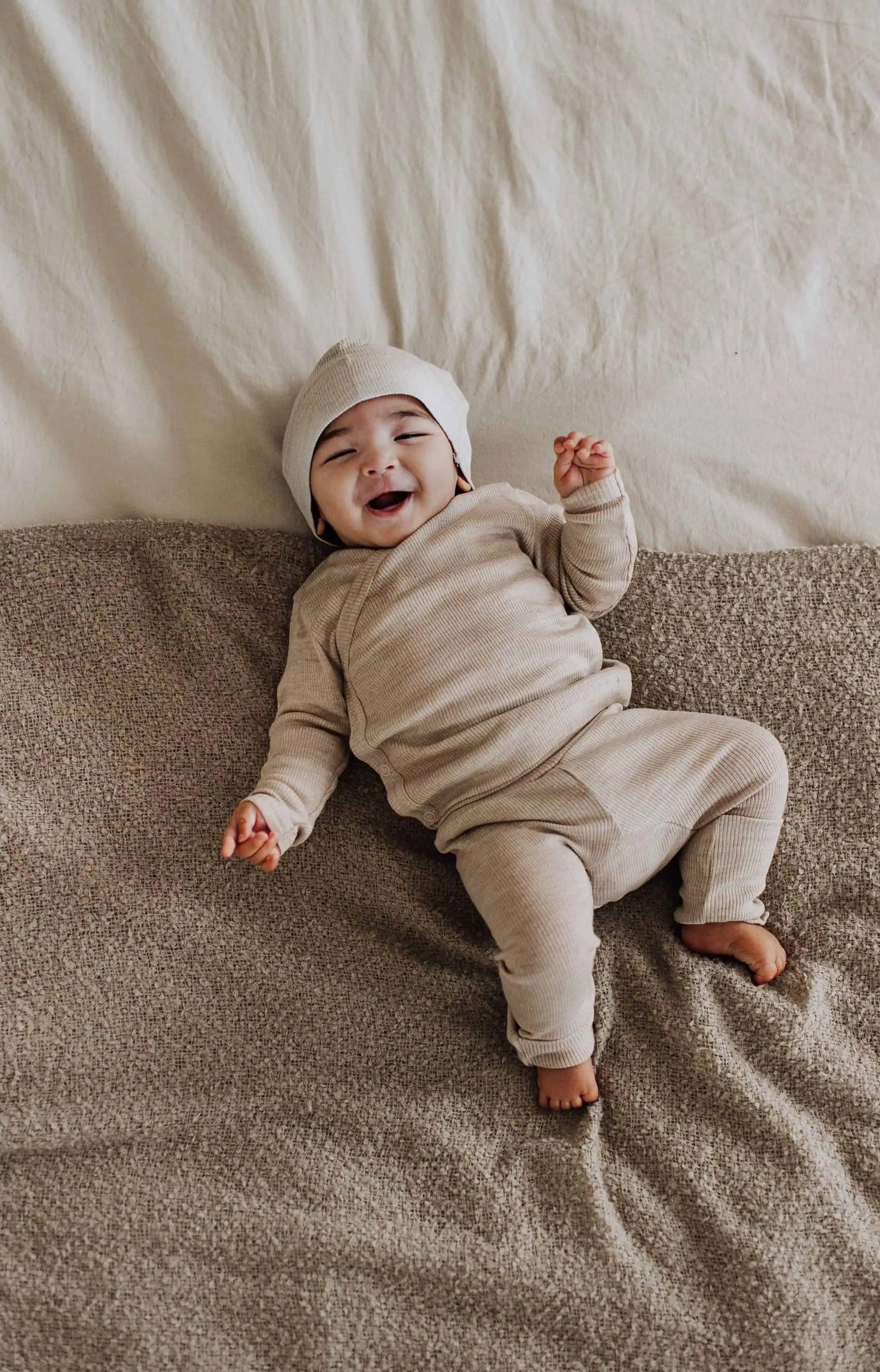 Lachende baby in wollenkleding met een legging, muts en overslagshirt met lange mouwen aan
