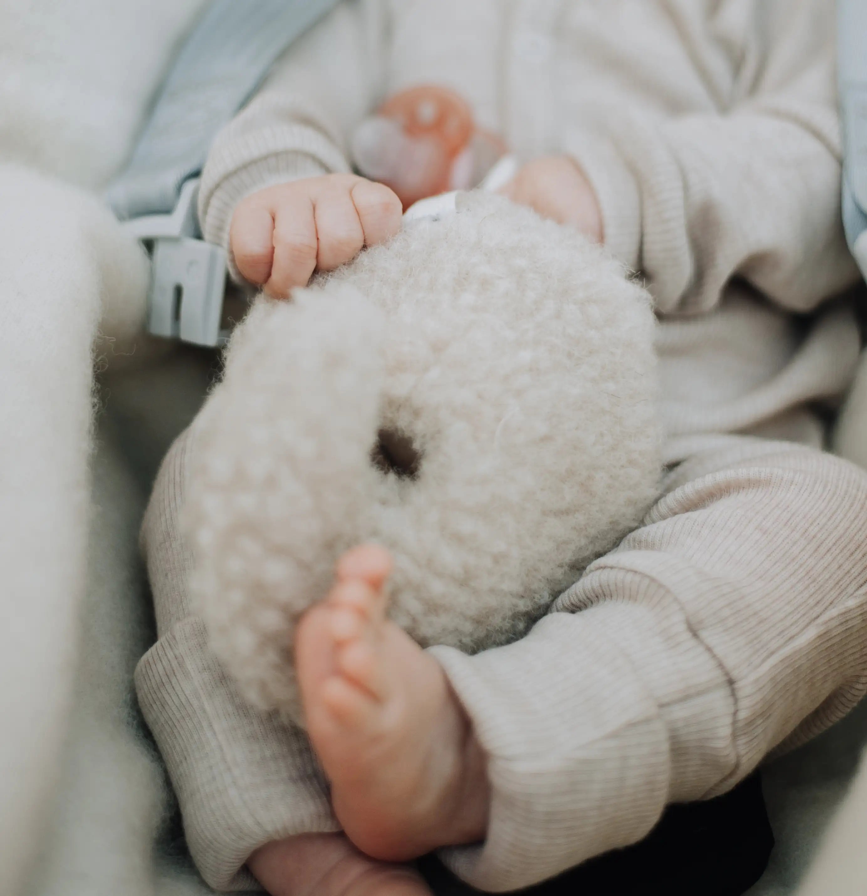 ingezoomde foto van een baby die ligt met een wollen knuffel tussen zijn benen