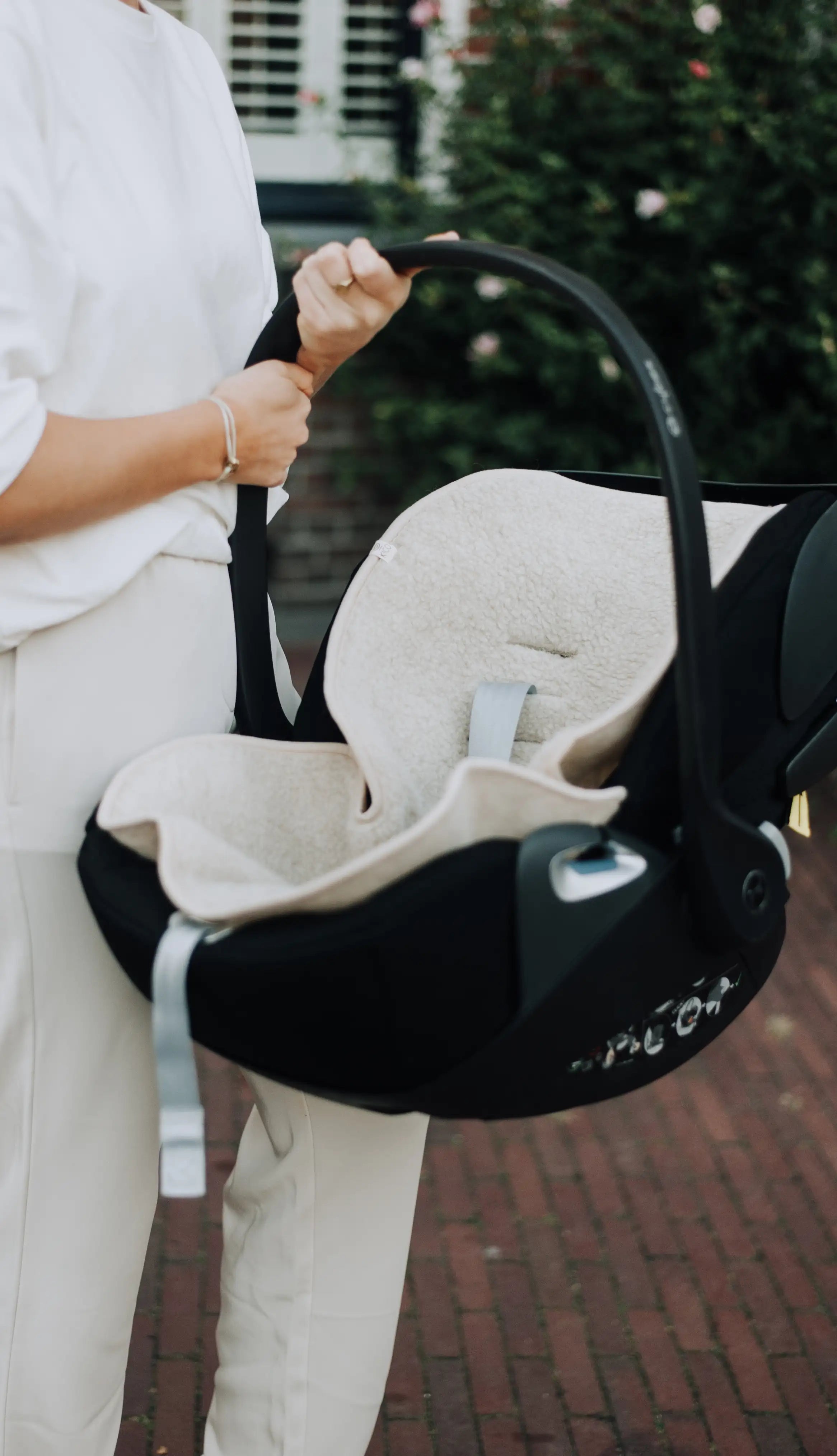 moeder die maxi cosi vast houdt met een wollen onderlegger waar een riempje doorheen zit