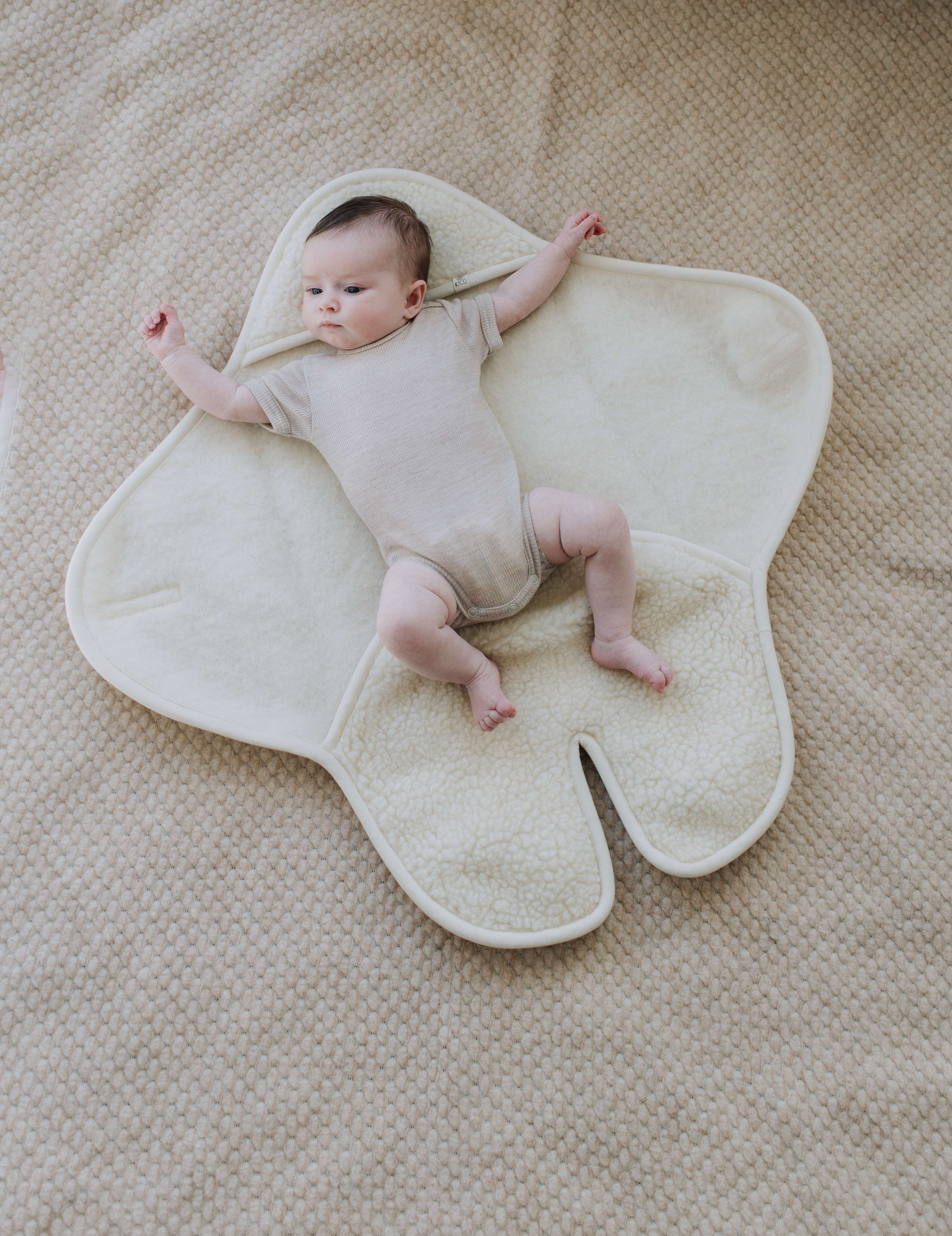 Baby met Kico Label romper uitgestrekt in een wikkeldeken met voetjes en capuchon